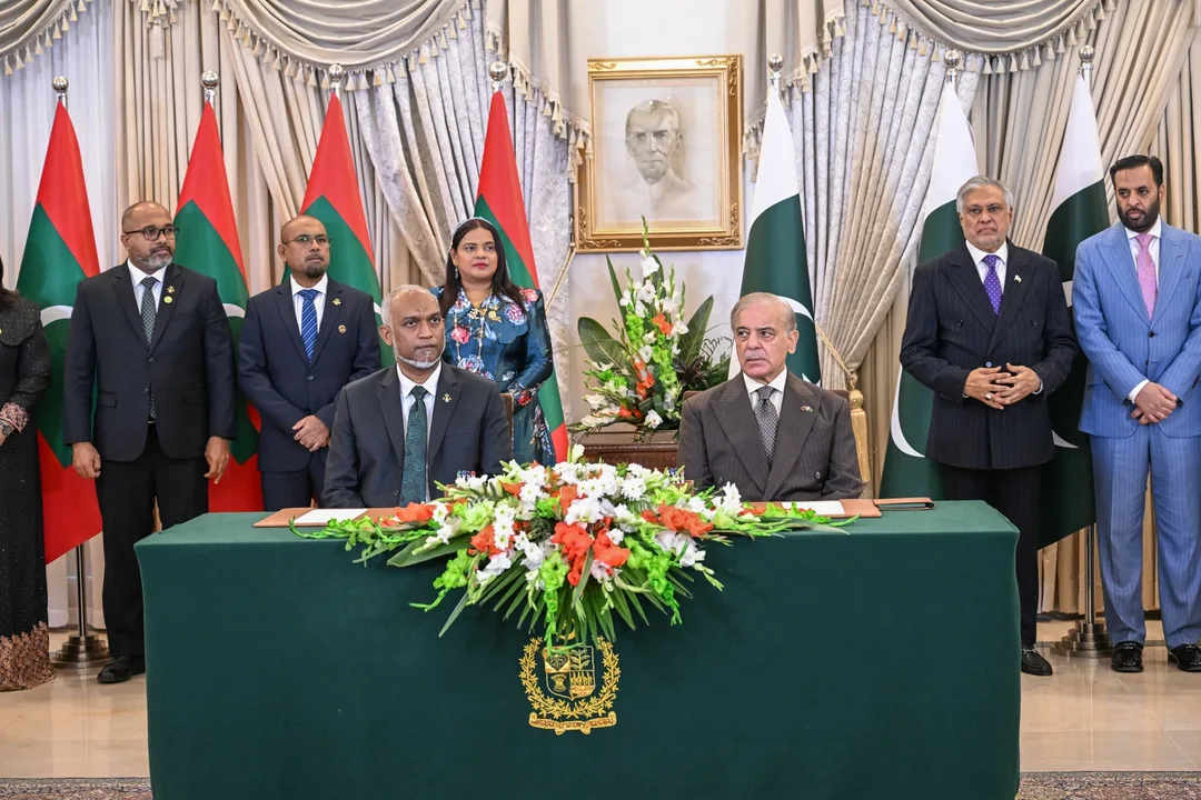 President Mohamed Muizzu and Pakistan's Prime Minister Shehbaz Sharif sit at a green-draped table with flowers, as officials stand behind them in front of Maldivian and Pakistani flags.