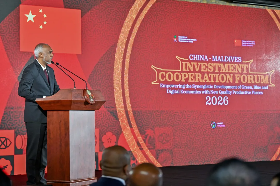 President Dr Mohamed Muizzu speaks at a wooden podium in front of a large red screen reading China–Maldives Investment Cooperation Forum 2026, with the Chinese flag shown behind him.